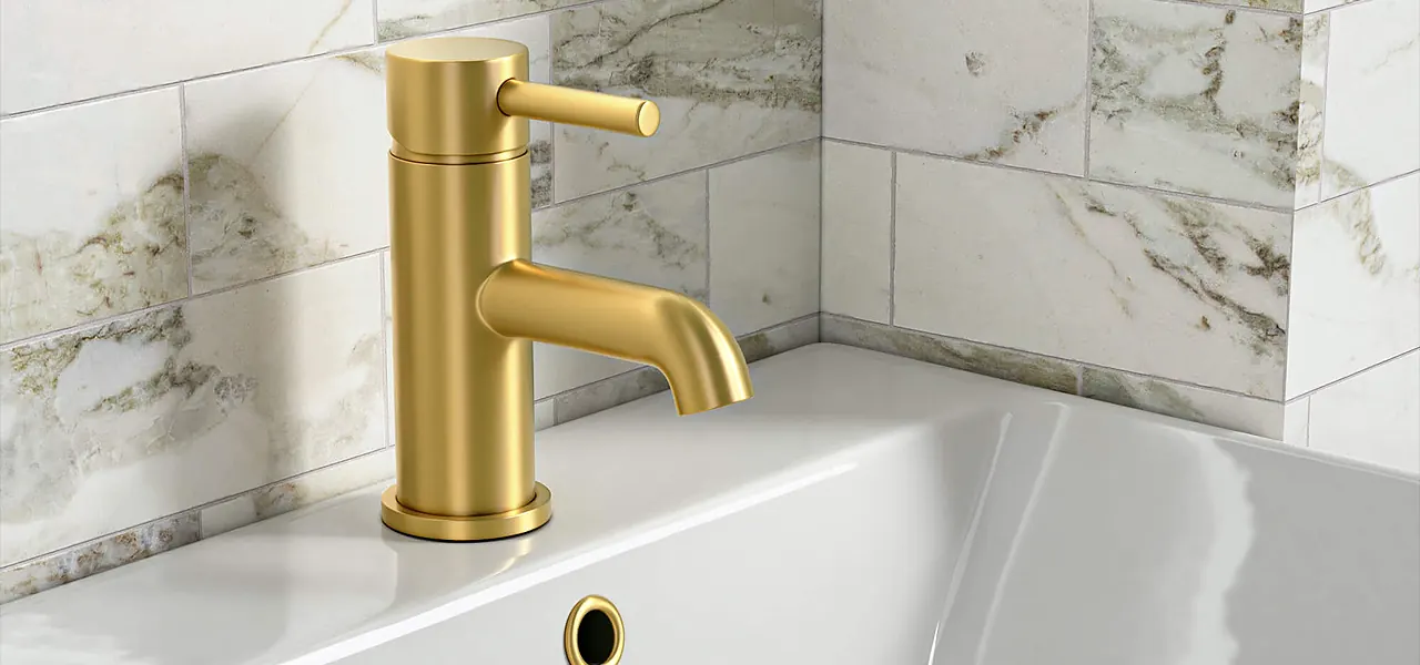 Brushed brass single-lever mono basin mixer tap on a white basin, against marble-effect tiles.