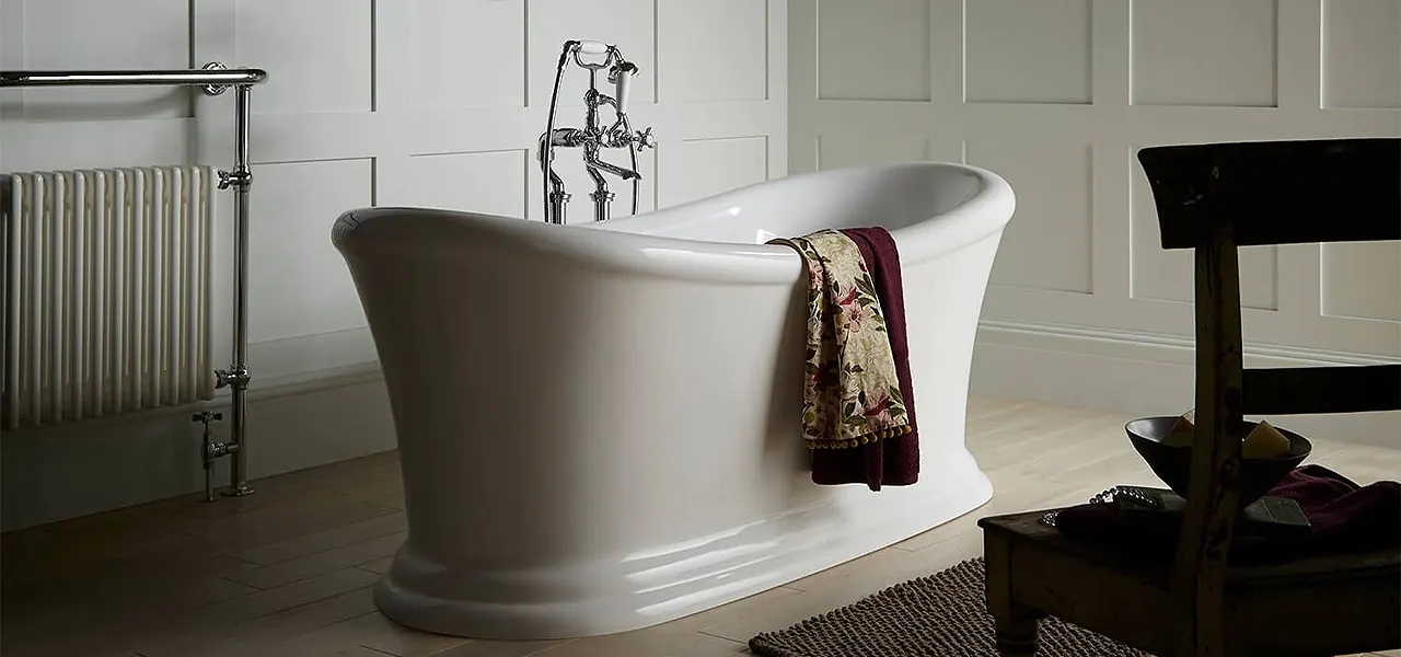 White double-ended bateau-style slipper bath with both ends raised, chrome bath-shower mixer taps and a floral towel, in a panelled bathroom.