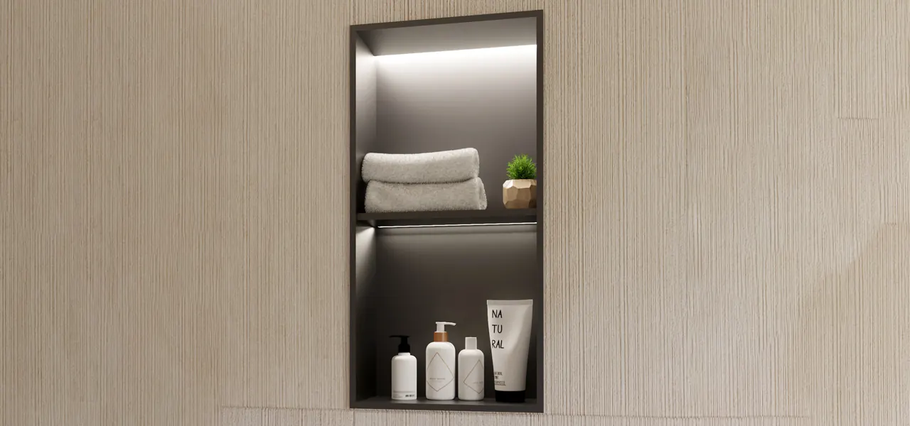 A tall vertical recessed shower niche divided into two compartments by a center shelf, with LED strip lighting illuminating folded gray towels and a small potted plant on top and three white toiletry bottles and a "Natural" tube on the bottom, set into a wood-textured wall.