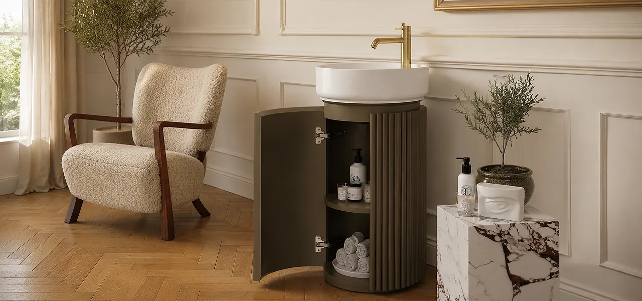 Fluted cylindrical floor-standing vanity unit in warm khaki with a round countertop basin and brushed brass tap, the curved door open to show shelved storage.