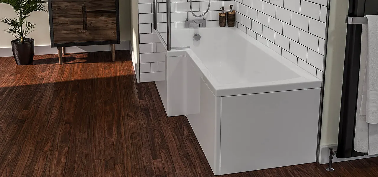 White L-shaped shower bath with a gloss front panel and chrome bath filler taps, against white metro tiles above a dark wood floor.