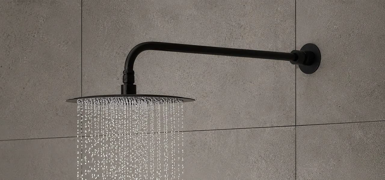 Matt black square rainfall shower head on a wall arm streaming water, against grey concrete-effect tiles.