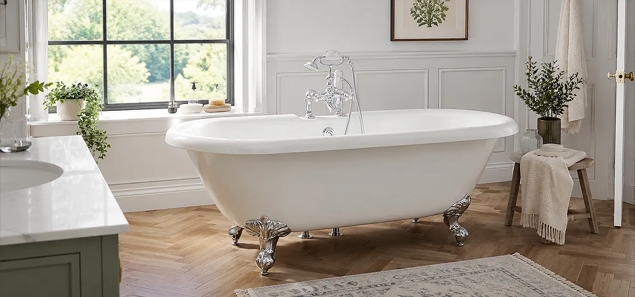 A traditional bathroom suite with a roll-top freestanding bath on black claw feet, a close-coupled toilet with a wooden seat, and a pedestal basin with chrome fittings, set in a period-style room with wood-beamed ceiling and cream wainscoting.