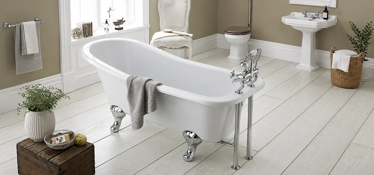 White acrylic roll-top slipper bath with a curved rim and chrome skirted feet, a grey towel draped over the side in a traditional bathroom.