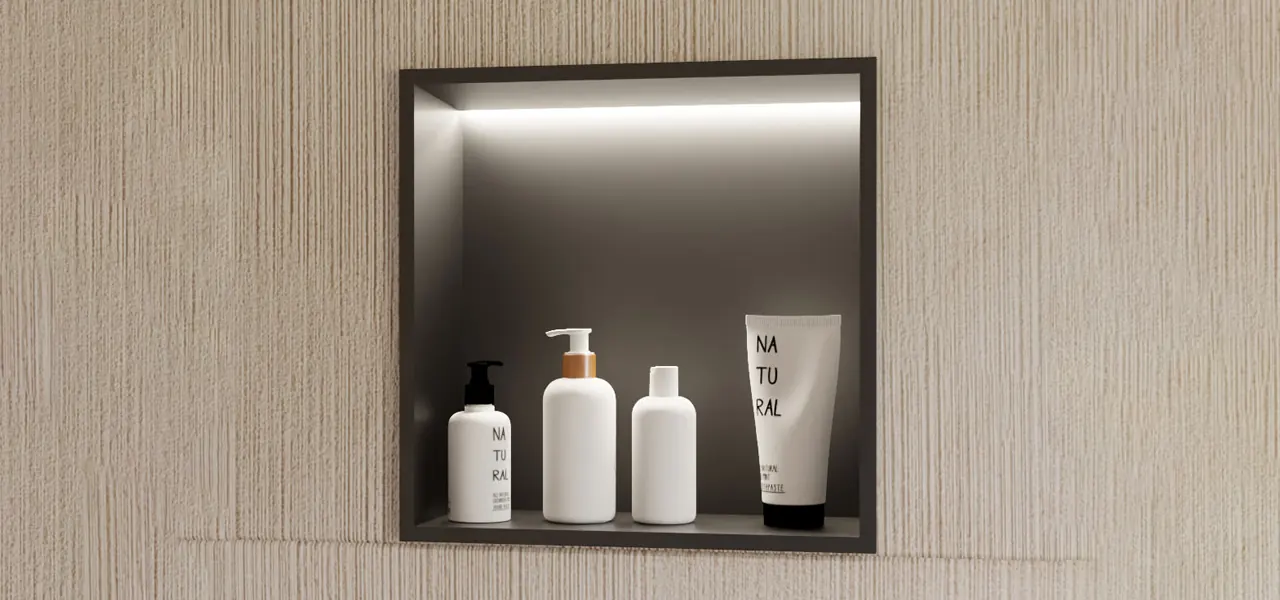 A square recessed shower niche with dark gray interior and integrated LED top lighting, holding four white "Natural" branded toiletry bottles and a tube, set into a light wood-textured wall.