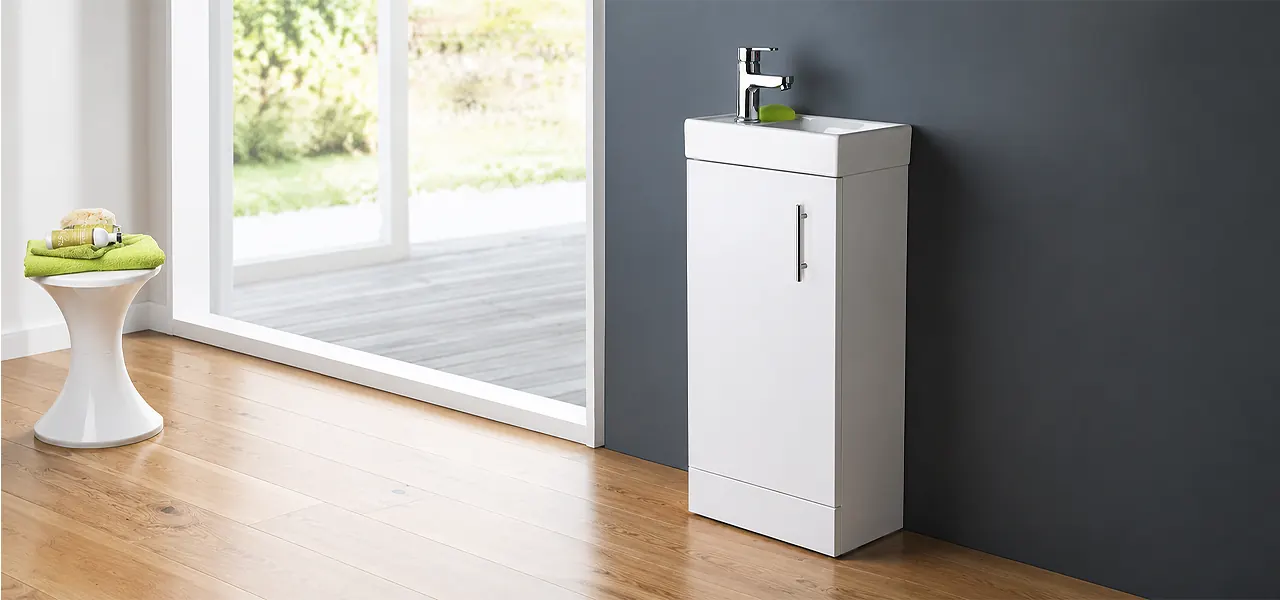 Compact white gloss floor-standing cloakroom vanity unit with a slim rectangular basin and chrome mono tap, against a grey wall on a wood floor.