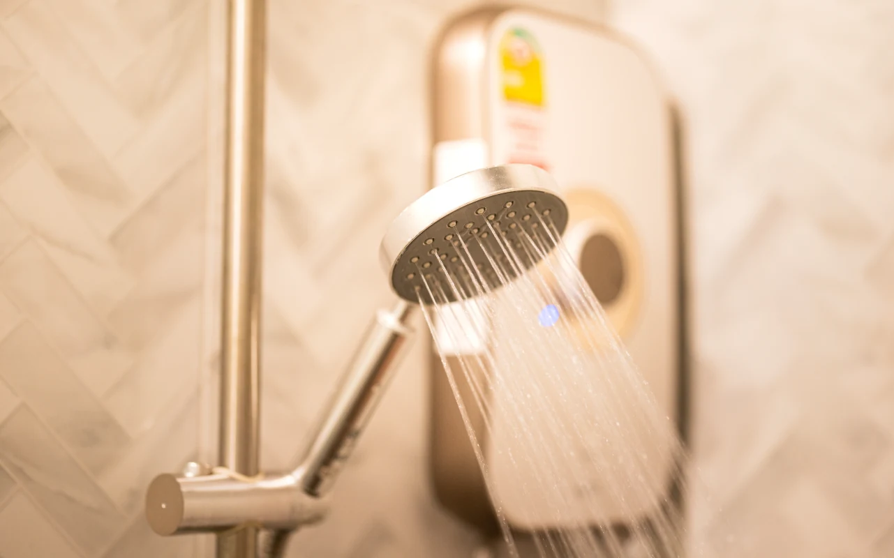 Close-up of a handheld shower head running hot water in front of an electric shower unit, illustrating on-demand heating and everyday electric shower use.