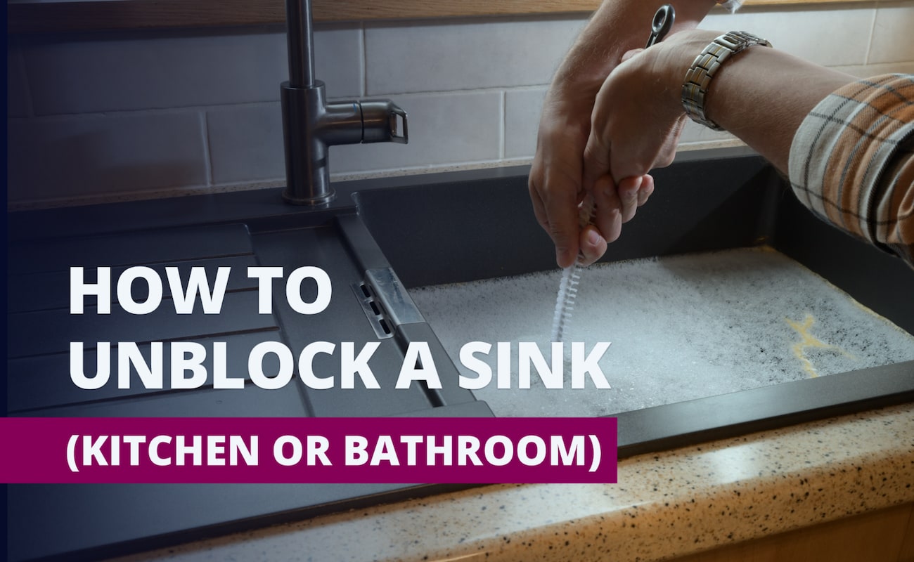 Person using a drain snake to unclog a kitchen sink filled with soapy water, with text overlay that reads “How to Unblock a Sink (Kitchen or Bathroom).”