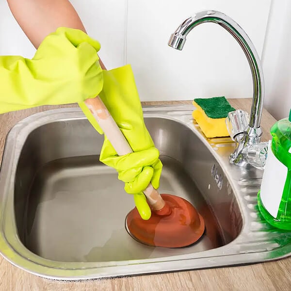 Clearing a blocked sink with a red rubber and wood plunger