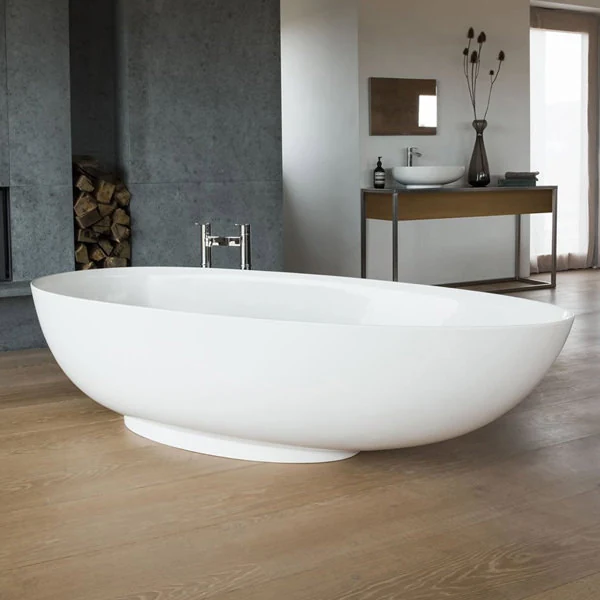 A modern oval freestanding bathtub with a smooth white finish, positioned on light wood flooring in a contemporary bathroom with minimalist décor and natural light.