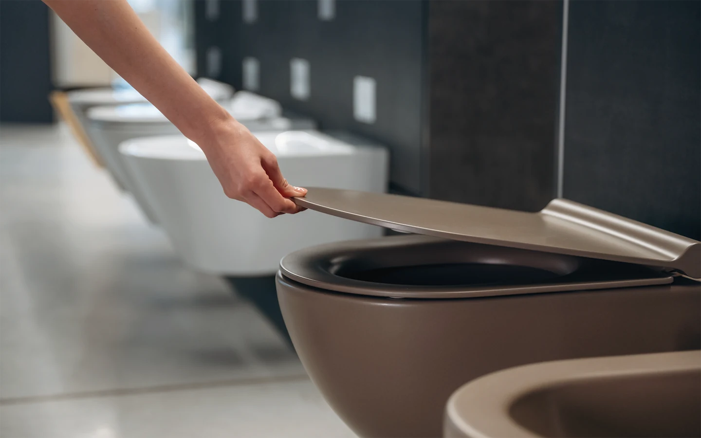 Close-up of a person lifting the lid of a brown wall-mounted smart toilet in a showroom.