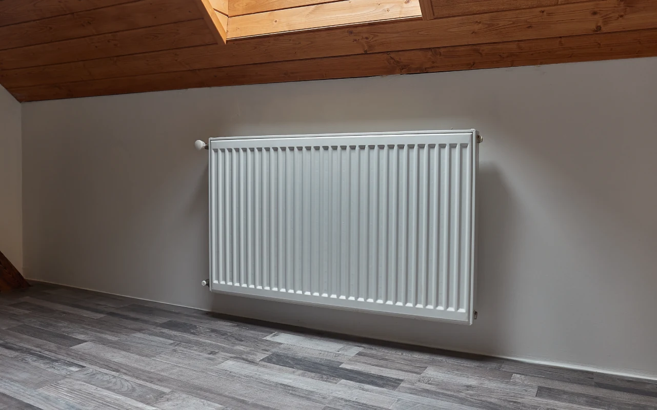 White panel radiator wall-mounted in a converted loft room with sloped wooden ceiling, illustrating how room volume and ceiling height affect BTU requirements