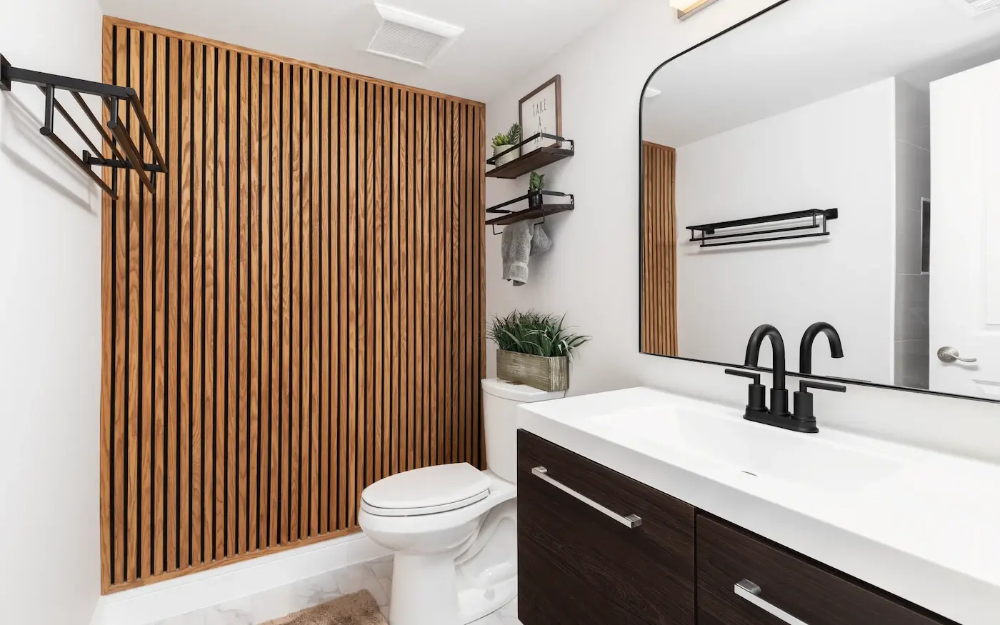 Modern bathroom with wood slat wall panels, black fixtures, and white vanity.